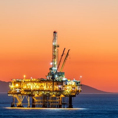 Offshore oil platform off the coast of California against a moody, orange sky as the sun sets behind the rig.